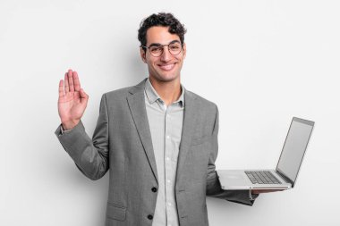 İspanyol yakışıklı adam mutlu bir şekilde gülümsüyor, el sallıyor, seni selamlıyor ve selamlıyor. iş ve dizüstü bilgisayar kavramı
