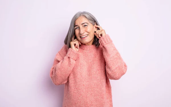 ストレス いらいらしそうな年配の女性が耳の両側を耳の聞こえない音や音や大きな音楽で覆い — ストック写真
