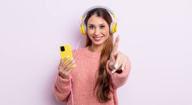 Asyalı güzel kadın gururla gülümsüyor ve kendinden emin bir numara oluyor. kulaklıklar ve telefon konsepti