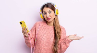 Asyalı güzel kadın şaşkın, şaşkın ve şüpheci hissediyor. kulaklıklar ve telefon konsepti