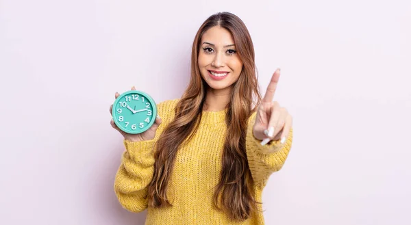アジア系の可愛い女性は笑顔で友好的で1位を示しています 目覚まし時計のコンセプト — ストック写真