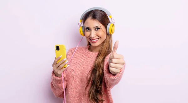 アジア系のきれいな女性は誇りを感じ 親指を上げて積極的に笑顔 ヘッドフォンと電話のコンセプト — ストック写真