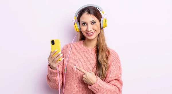 アジア系の可愛い女は陽気に笑って幸せを感じ横を指差してる ヘッドフォンと電話のコンセプト — ストック写真