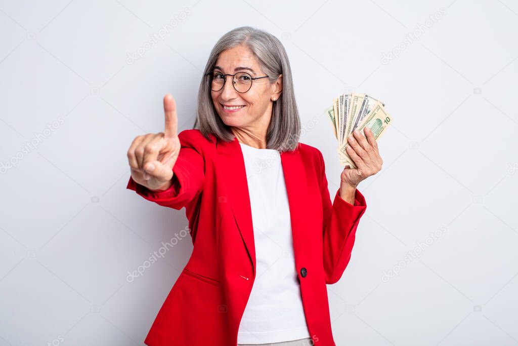 senior pretty woman smiling proudly and confidently making number one. business and banknotes concept