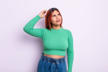 Genç İspanyol kadın şaşkın ve şaşkın hissediyor, kafasını kaşıyor ve yan tarafa bakıyor.