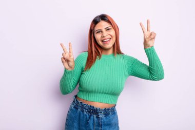 Genç İspanyol kadın gülümsüyor ve mutlu görünüyor, arkadaş canlısı ve tatmin olmuş, zafer ya da barış işareti yapıyor.