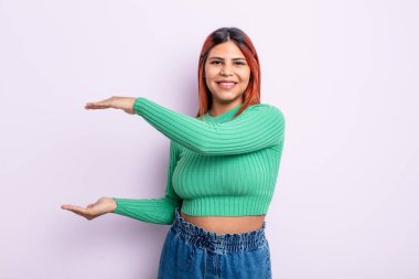 Genç İspanyol kadın gülümsüyor, mutlu, pozitif ve memnun, fotokopi alanında nesne ya da konsept tutuyor ya da gösteriyor