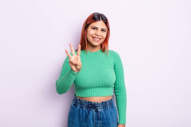 Genç İspanyol kadın gülümsüyor ve arkadaş canlısı görünüyor. Üç ya da üç numarayı gösteriyor. Elleri önde, geri sayıyor.