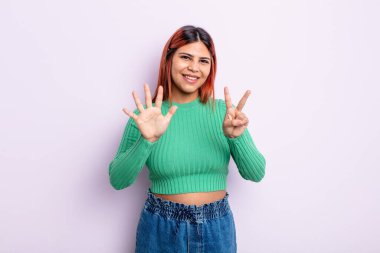 Genç İspanyol kadın gülümsüyor ve dost canlısı görünüyor, 7 ya da 7 numarayı gösteriyor, eli önde, geri sayıyor.