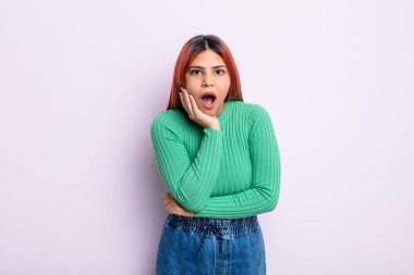 Genç İspanyol kadın şok ve inançsızlıkla ağzı açık, elleri yanak ve kolları çapraz, sersemlemiş ve şaşırmış hissediyor.