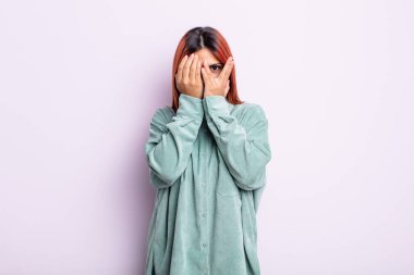 Latin kökenli genç bir kadın korkmuş ya da utanmış hissediyor. Gözleri yarı kapalı ya da elleri kapalı gözetliyor.