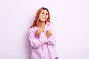 Genç İspanyol kadın sevinçle gülümsüyor ve kutluyor, yumruklarını sıkmış ve kollarını kavuşturmuş, mutlu ve pozitif hissediyor.