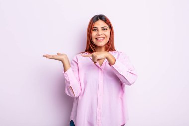 Genç İspanyol kadın neşeyle gülümsüyor ve yan taraftaki fotokopi alanını işaret ediyor, bir nesneyi gösteriyor ya da reklamını yapıyor.