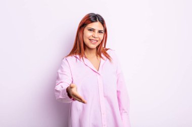 Genç İspanyol kadın gülümsüyor, mutlu, kendinden emin ve arkadaş canlısı görünüyor, bir anlaşmaya varmak için el sıkışmayı teklif ediyor, işbirliği yapıyor.