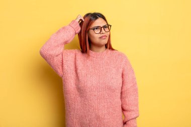 Genç İspanyol kadın şaşkın ve şaşkın hissediyor, kafasını kaşıyor ve yan tarafa bakıyor.