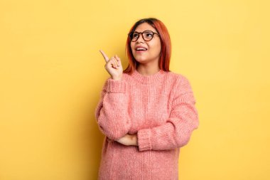 Genç İspanyol kadın mutlu bir şekilde gülümsüyor ve yan bakıyor, merak ediyor, düşünüyor ya da bir fikri var.