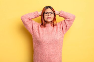 Genç İspanyol kadın kendini stresli, endişeli, endişeli ya da korkmuş hissediyor. Elleri başının üstünde, hatayla panikliyor.