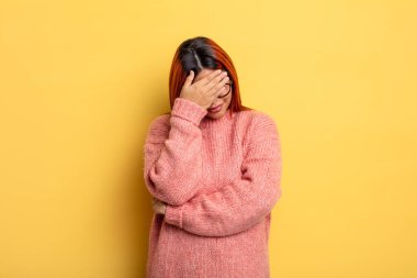 Genç İspanyol kadın stresli, utanmış ya da üzgün görünüyor, baş ağrısı var, yüzünü eliyle kapatıyor.