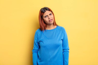 young hispanic woman feeling puzzled and confused, with a dumb, stunned expression looking at something unexpected