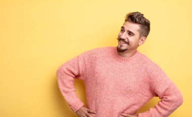 Genç yakışıklı adam mutlu, neşeli ve kendinden emin görünüyor, gururla gülümsüyor ve iki elini de kalçasında görmek istiyor. Garip bıyık konsepti