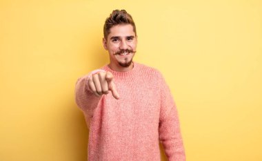 Genç yakışıklı bir adam kameraya bakıyor, kendinden emin, arkadaş canlısı bir gülümsemeyle, seni seçiyor. Garip bıyık konsepti