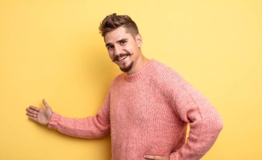 Genç yakışıklı adam kendini mutlu ve neşeli hissediyor, gülümsüyor ve seni hoş karşılıyor, dostça bir jestle içeri davet ediyor. Garip bıyık konsepti