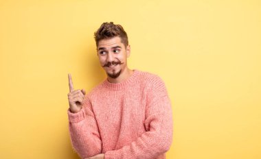 Genç yakışıklı adam mutlu bir şekilde gülümsüyor ve yan bakıyor, merak ediyor, düşünüyor ya da bir fikri var. Garip bıyık konsepti