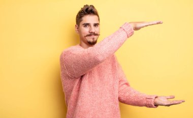 Genç yakışıklı adam gülümsüyor, mutlu, pozitif ve tatmin olmuş hissediyor, fotokopi alanında nesne ya da konsept tutuyor ya da gösteriyor. Garip bıyık konsepti