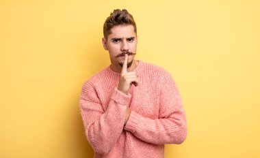 Genç ve yakışıklı bir adam ciddi görünüyor ve parmaklarını dudaklarına bastırıp sessizlik ya da sessizlik talep ediyor, sır saklıyor. Garip bıyık konsepti