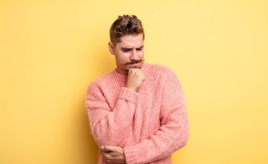 Genç ve yakışıklı bir adam ciddi, düşünceli ve endişeli, elleri çenesine bastırılmış bir şekilde yan bakıyor. Garip bıyık konsepti