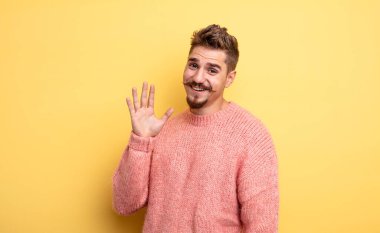 Genç yakışıklı adam mutlu ve neşeli bir şekilde gülümsüyor, el sallıyor, sizi selamlıyor ve selamlıyor, ya da veda ediyor. Garip bıyık konsepti