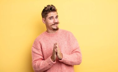 Genç yakışıklı adam mutlu ve başarılı hissediyor, gülümsüyor ve alkışlıyor, alkışlarla tebrik ediyor. Garip bıyık konsepti