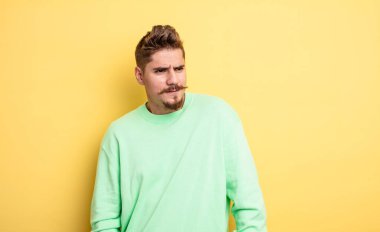 Genç, yakışıklı bir adam üzgün, üzgün ya da kızgın ve olumsuz bir tavır takınıyor, anlaşmazlık içinde kaşlarını çatıyor. Garip bıyık konsepti