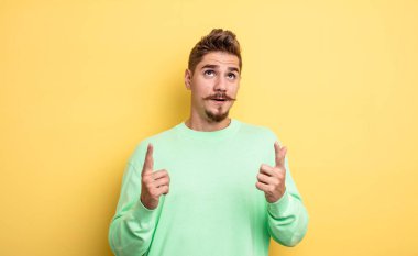 Genç yakışıklı adam şaşırmış, şaşırmış ve ağzı açık görünüyor, iki eliyle uzayı kopyalamak için yukarı bakıyor. Garip bıyık konsepti