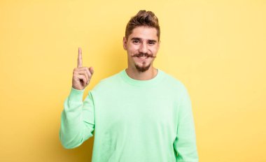 Genç ve yakışıklı bir adam mutlu bir şekilde gülümsüyor, tek eliyle yukarıyı işaret ederek boşluğu kopyalıyor. Garip bıyık konsepti