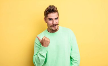 Genç ve yakışıklı bir adam inançsızlıktan şaşkın şaşkın bakıyor, yan taraftaki objeyi işaret ediyor ve 
