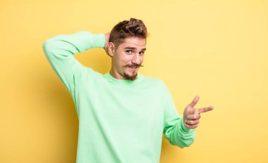 Genç yakışıklı adam gülüyor, mutlu, pozitif ve şaşırmış görünüyor, yanal fotokopi alanını işaret eden harika bir fikrin farkına varıyor. Garip bıyık konsepti