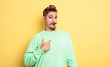 Şok olmuş ve ağzı açık, kendini işaret eden genç ve yakışıklı bir adam. Garip bıyık konsepti