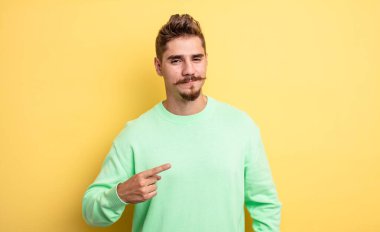 Genç yakışıklı, gururlu, kendine güvenen ve mutlu görünen, gülümseyen ve kendini gösteren ya da bir numara işareti yapan bir adam. Garip bıyık konsepti