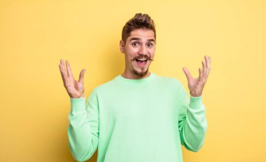 Genç yakışıklı adam mutlu ve heyecanlı görünüyor. Beklenmedik bir sürprizle şoke olmuş. İki eli de yüzü açık. Garip bıyık konsepti