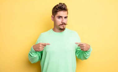 Genç, yakışıklı, gururlu, pozitif ve iki elinle göğsünü gösteren bir adam. Garip bıyık konsepti