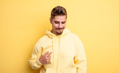 Genç yakışıklı adam neşeyle ve gelişigüzel gülümsüyor, aşağıya bakıyor ve göğsünü işaret ediyor. Garip bıyık konsepti