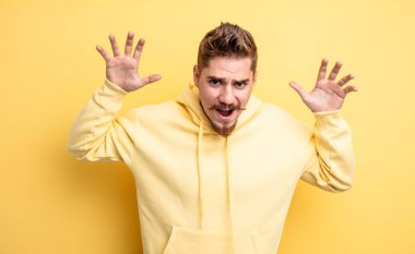 Genç ve yakışıklı bir adam panik ya da öfke içinde bağırıyor. Şok olmuş, korkmuş ya da öfkeli. Elleri başının yanında. Garip bıyık konsepti