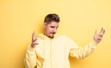 young handsome man shrugging with a dumb, crazy, confused, puzzled expression, feeling annoyed and clueless. strange moustache concept