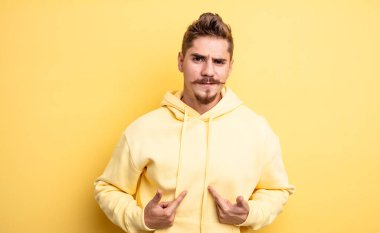 Genç yakışıklı adam, kafası karışmış ve tuhaf bakışlarıyla kendini işaret ediyor. Seçildiğine şaşırmış ve şaşırmış. Garip bıyık konsepti