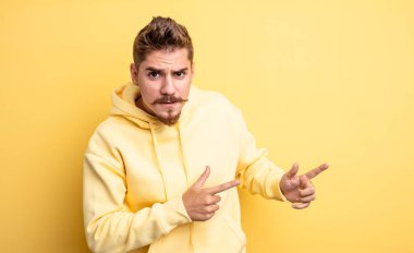 Genç yakışıklı bir adam şaşkın ve şaşırmış hissediyor. Kenardaki fotokopi alanını işaret ediyor. Şaşırmış, ağzı açık bir bakışla. Garip bıyık konsepti