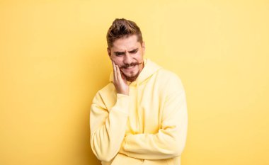 Genç yakışıklı adam yanağını tutuyor ve ağrılı diş ağrısı çekiyor, hasta, sefil ve mutsuz hissediyor, dişçi arıyor. Garip bıyık konsepti