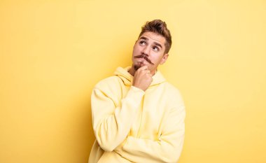 Genç yakışıklı adam düşünceli, meraklı ya da hayal kuruyor, hayal kuruyor ve mekanı kopyalamak için yukarı bakıyor. Garip bıyık konsepti