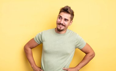 Genç yakışıklı adam mutlu, neşeli ve kendinden emin görünüyor, gururla gülümsüyor ve iki elini de kalçasında görmek istiyor. Garip bıyık konsepti