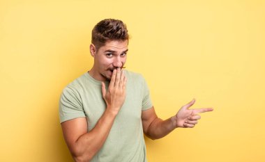 Genç yakışıklı adam kendini mutlu, şok olmuş ve şaşırmış hissediyor. Ağzını eliyle kapatıyor ve yanal kopya alanını işaret ediyor. Garip bıyık konsepti